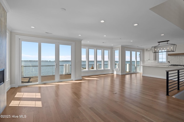 unfurnished living room with recessed lighting, light wood-type flooring, crown molding, and an inviting chandelier