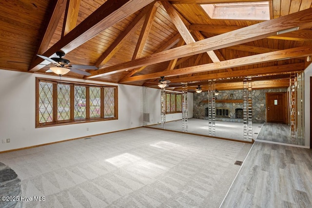 unfurnished living room featuring a skylight, baseboards, beam ceiling, and a stone fireplace