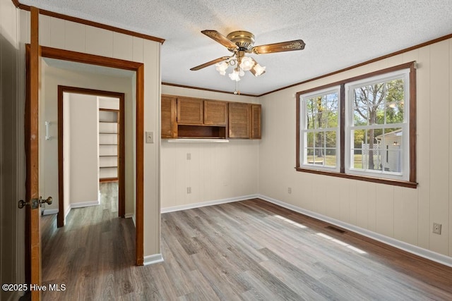 interior space with crown molding, visible vents, a ceiling fan, and wood finished floors