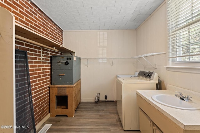 laundry area with a sink, brick wall, visible vents, washing machine and clothes dryer, and wood finished floors