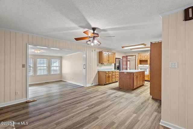 kitchen with a center island, stainless steel fridge, light countertops, a ceiling fan, and light wood finished floors