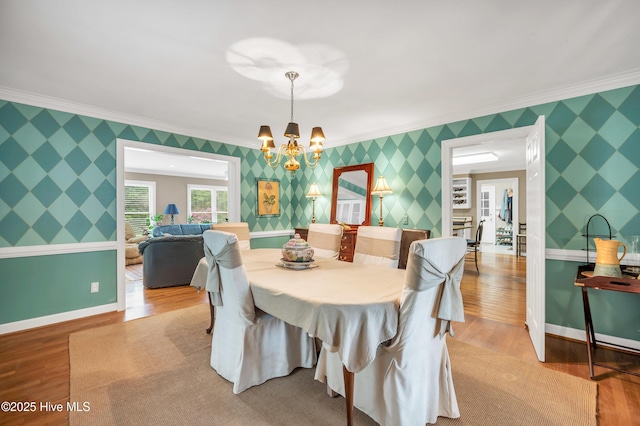 dining room featuring ornamental molding, wallpapered walls, a chandelier, wood finished floors, and baseboards