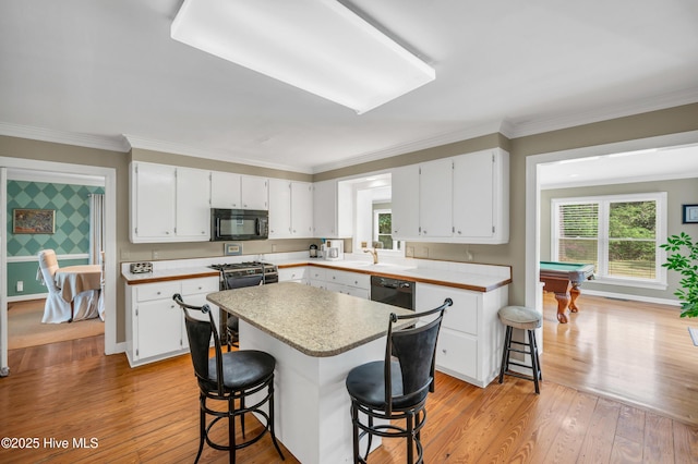 kitchen featuring black appliances, white cabinetry, light wood-style floors, a breakfast bar, and ornamental molding