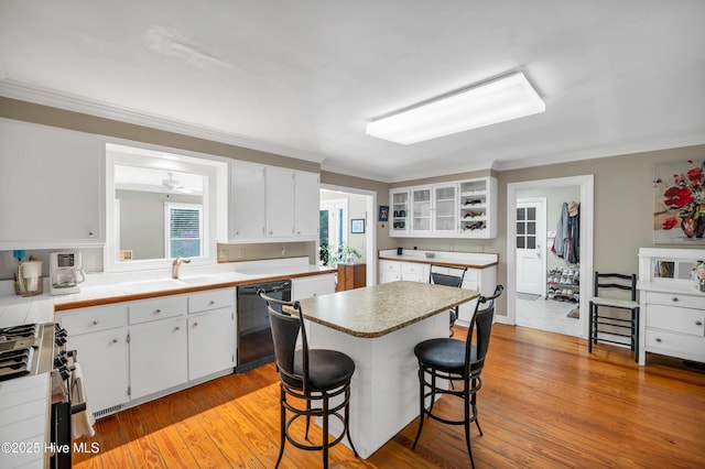 kitchen featuring dishwasher, stainless steel gas stove, white cabinets, ornamental molding, and a breakfast bar