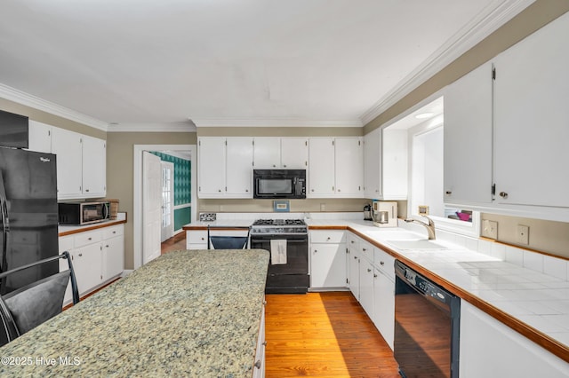 kitchen with black appliances, a sink, crown molding, light wood-style floors, and light countertops