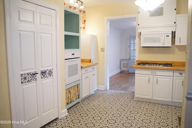 kitchen with white appliances, baseboards, light floors, white cabinets, and wood counters