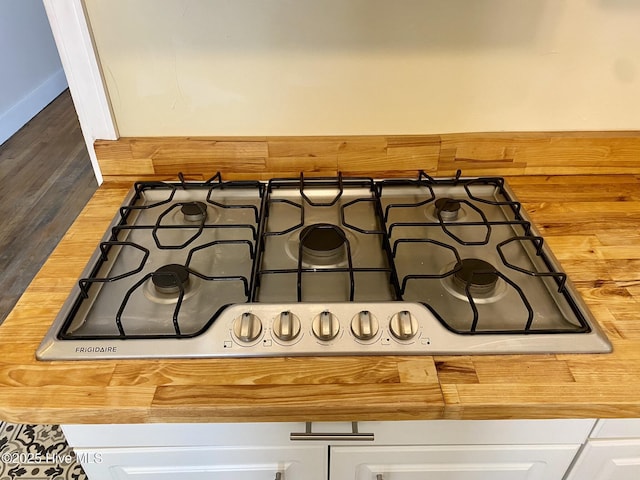 interior details featuring butcher block countertops, stainless steel gas cooktop, and white cabinets