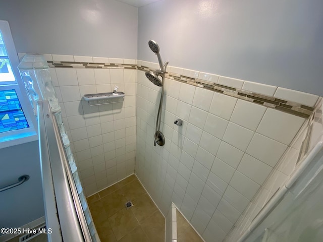 bathroom with wainscoting, tile walls, a tile shower, and tile patterned flooring