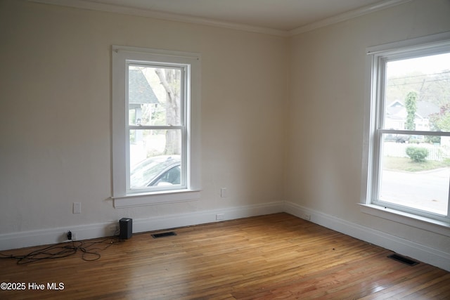 empty room with visible vents, plenty of natural light, ornamental molding, and light wood-style floors