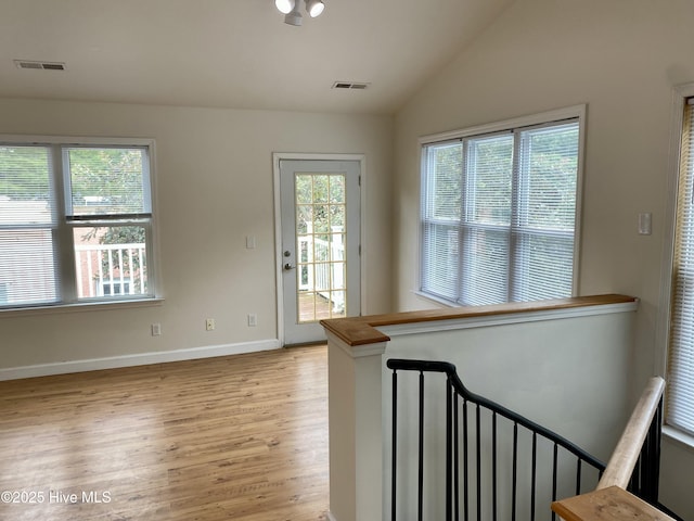 interior space featuring light wood-style floors, baseboards, lofted ceiling, and visible vents