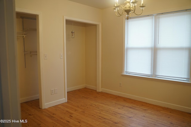 unfurnished bedroom featuring a notable chandelier, a walk in closet, light wood-style flooring, baseboards, and a closet
