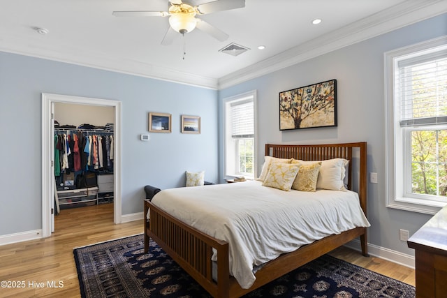 bedroom featuring ornamental molding, visible vents, a walk in closet, and light wood-style floors