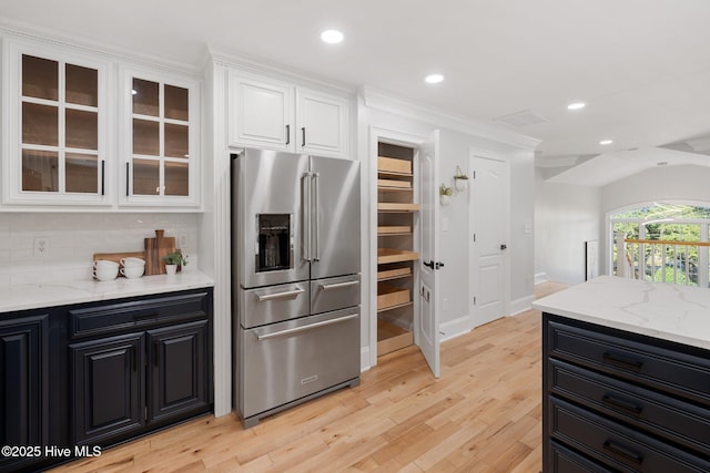 kitchen featuring white cabinets, light wood finished floors, light stone counters, high end fridge, and tasteful backsplash
