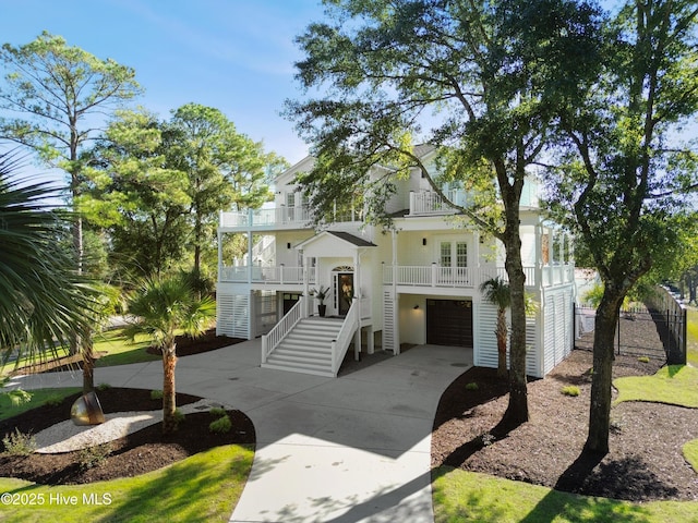coastal home with french doors, driveway, an attached garage, stairs, and a balcony