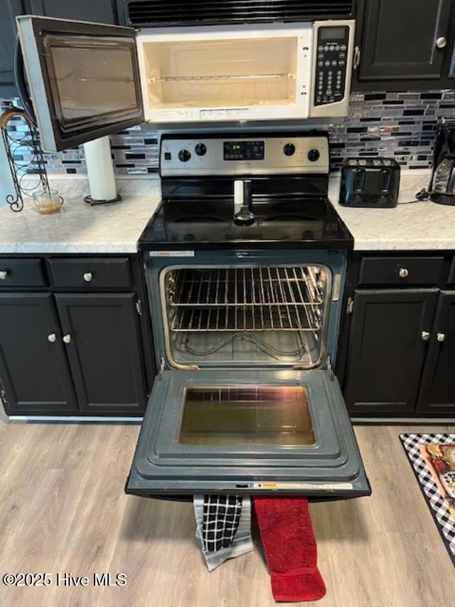 kitchen featuring electric stove, light wood-type flooring, dark cabinetry, and backsplash
