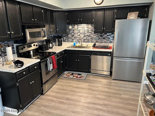kitchen with dark cabinetry, a sink, appliances with stainless steel finishes, and light wood-style floors