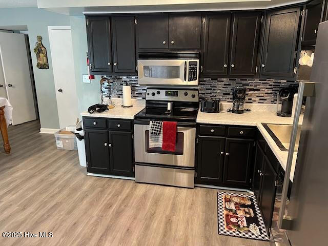 kitchen featuring light wood-style flooring, stainless steel appliances, and dark cabinets