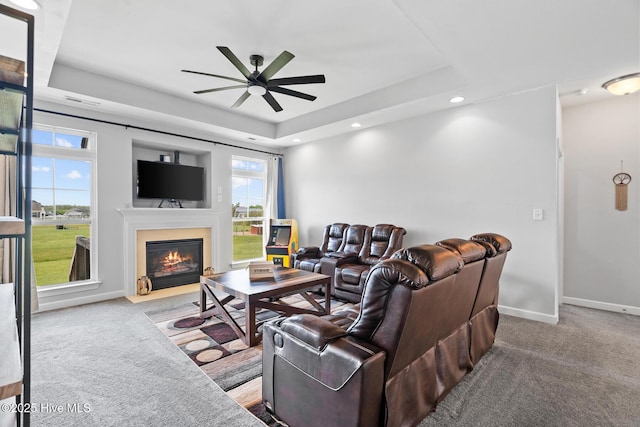 carpeted living room with baseboards, recessed lighting, a ceiling fan, a fireplace with flush hearth, and a raised ceiling