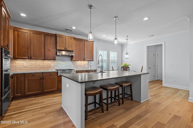 kitchen featuring a sink, a kitchen bar, decorative backsplash, crown molding, and under cabinet range hood