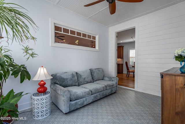 living area with carpet floors, a ceiling fan, baseboards, and wood walls