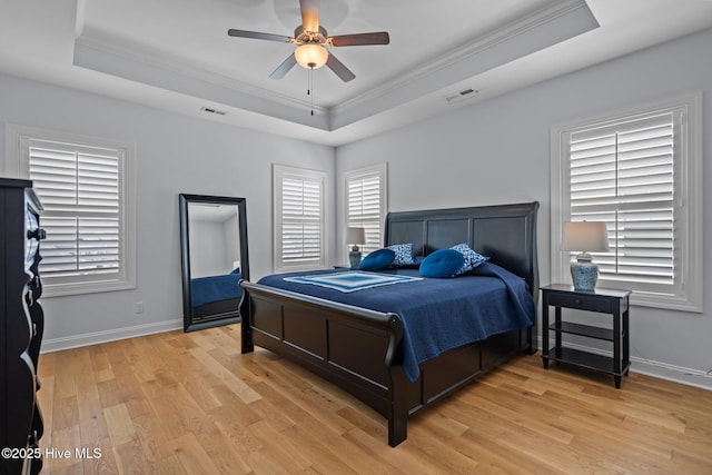 bedroom with visible vents, a tray ceiling, light wood-type flooring, and crown molding