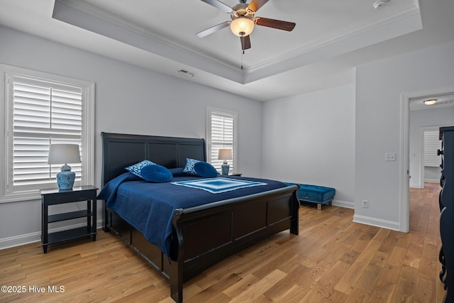 bedroom featuring light wood finished floors, a tray ceiling, visible vents, crown molding, and baseboards