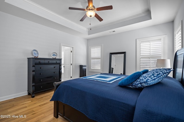 bedroom featuring a tray ceiling, multiple windows, light wood-style flooring, and ornamental molding