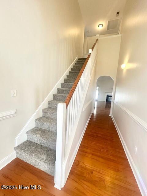 stairway featuring arched walkways, baseboards, and wood finished floors