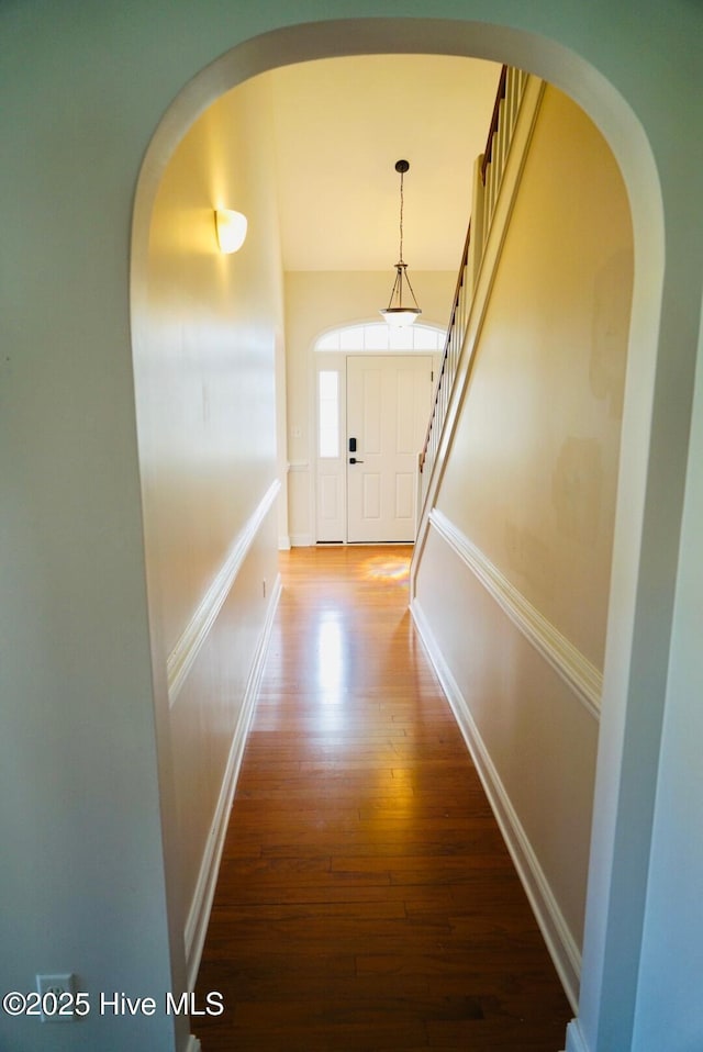 hallway with arched walkways, baseboards, stairs, and wood finished floors