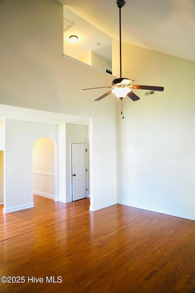unfurnished room with baseboards, a ceiling fan, arched walkways, and wood finished floors