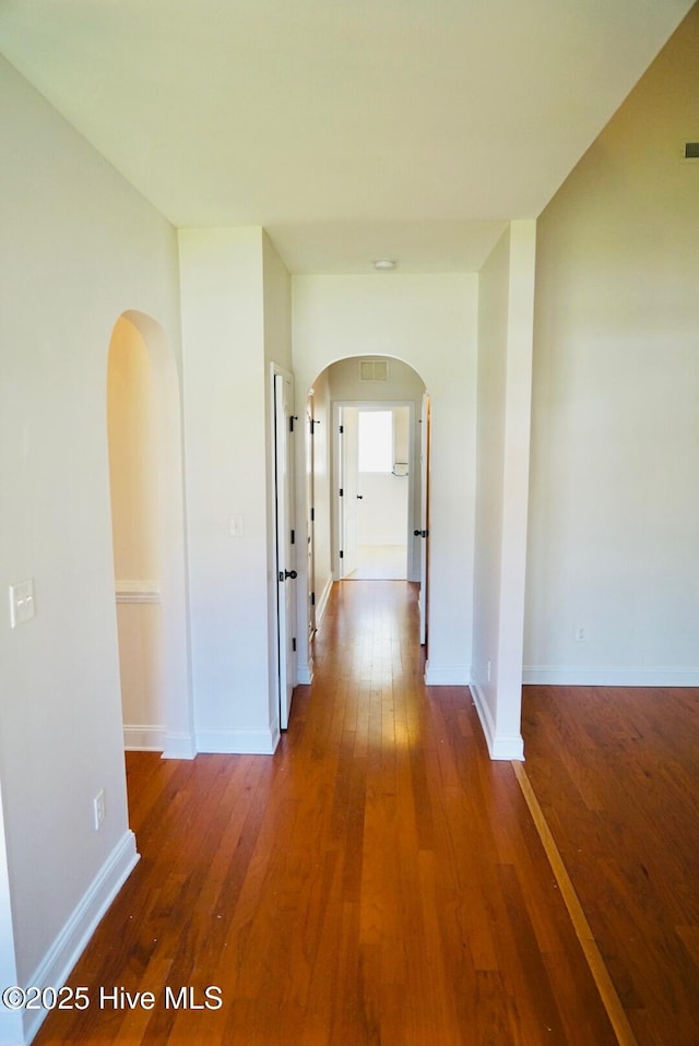 hall featuring arched walkways, baseboards, wood finished floors, and visible vents