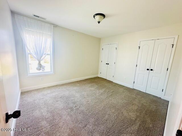 unfurnished bedroom featuring visible vents, baseboards, carpet floors, and two closets