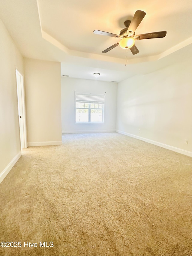 spare room featuring baseboards, a ceiling fan, a raised ceiling, and light carpet