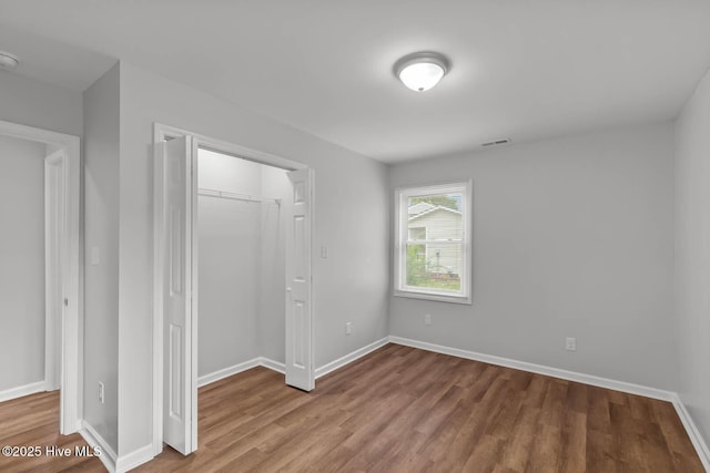 unfurnished bedroom with visible vents, baseboards, a closet, and wood finished floors