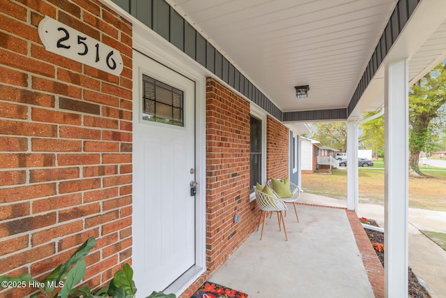 doorway to property with brick siding, a porch, and board and batten siding
