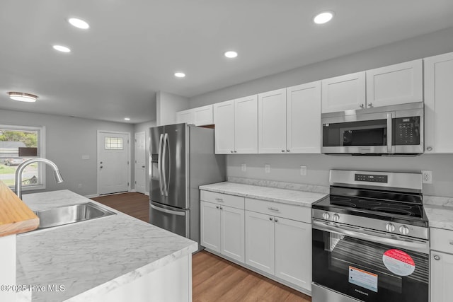 kitchen featuring white cabinets, a sink, light wood-type flooring, recessed lighting, and stainless steel appliances