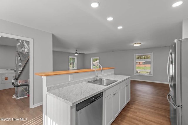 kitchen with white cabinetry, a kitchen island with sink, a sink, washer / dryer, and stainless steel appliances