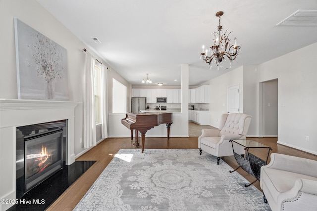 living area featuring visible vents, an inviting chandelier, wood finished floors, and a fireplace with flush hearth