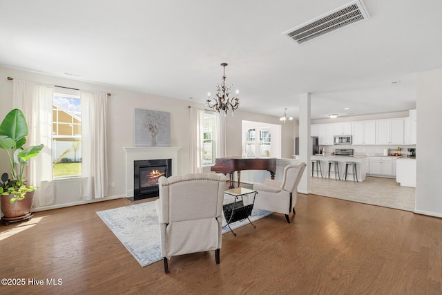 living room with a chandelier, light wood-style floors, visible vents, and a wealth of natural light