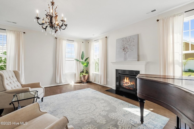 sitting room featuring a chandelier, a fireplace with flush hearth, visible vents, and wood finished floors
