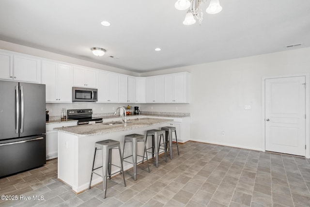 kitchen with a sink, a kitchen bar, a center island with sink, light stone counters, and stainless steel appliances