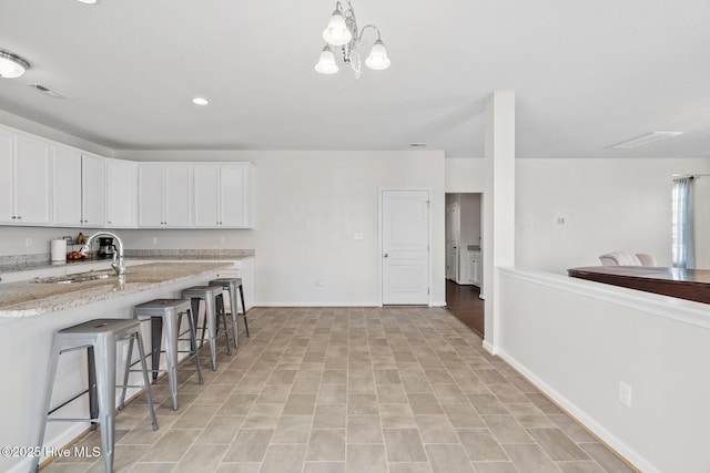 kitchen with light stone countertops, a kitchen bar, white cabinets, a sink, and baseboards
