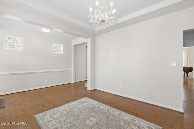 empty room with crown molding, baseboards, a chandelier, and wood finished floors