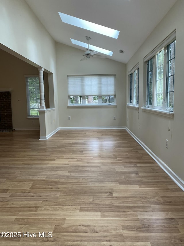 unfurnished room with vaulted ceiling with skylight, a ceiling fan, visible vents, wood finished floors, and baseboards