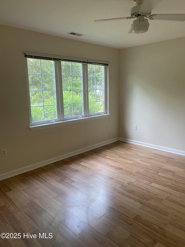 empty room featuring visible vents, ceiling fan, wood finished floors, and a wealth of natural light