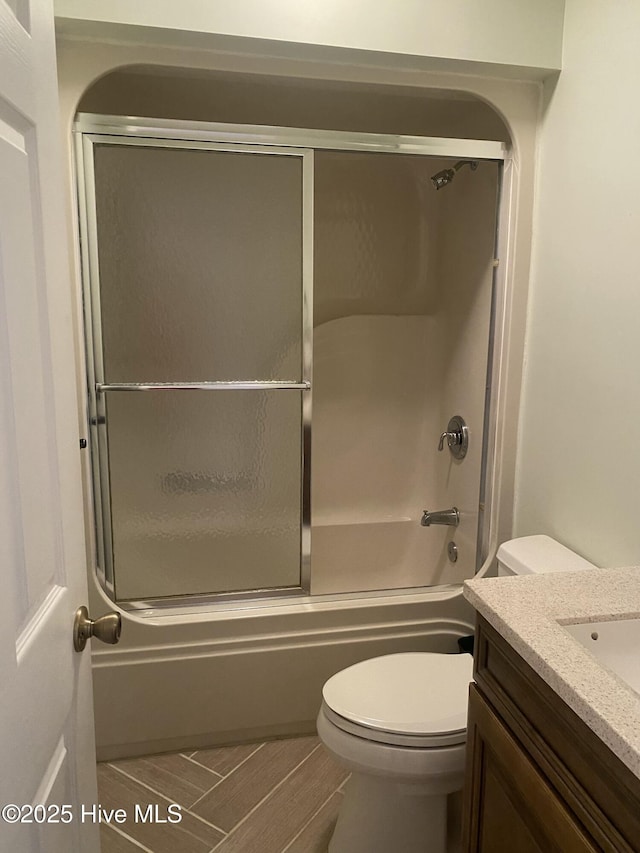 full bathroom with toilet, wood finished floors, bath / shower combo with glass door, and vanity