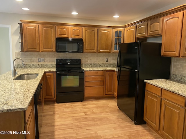 kitchen with light wood-style floors, tasteful backsplash, light stone counters, a sink, and black appliances