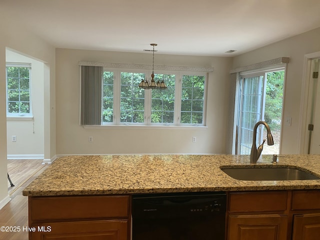 kitchen with pendant lighting, wood finished floors, dishwasher, a sink, and light stone counters