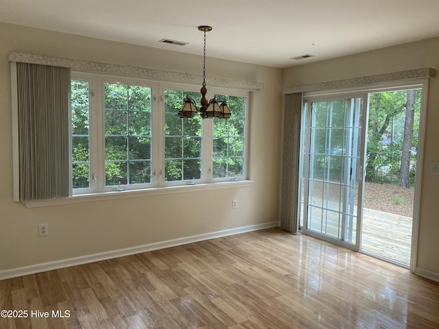 unfurnished dining area featuring an inviting chandelier, baseboards, wood finished floors, and visible vents