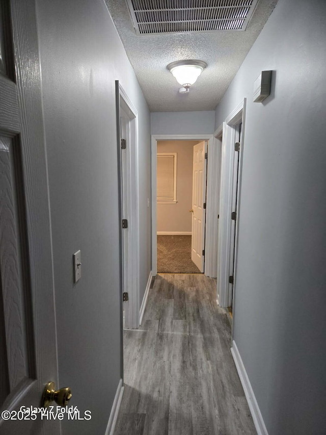 hall featuring wood finished floors, visible vents, baseboards, and a textured ceiling